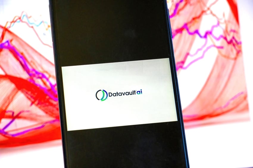 DataVaultAI logo displayed in foreground on mobile phone with stock chart in background on computer screen
