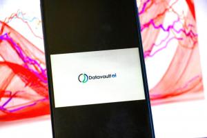 DataVaultAI logo displayed in foreground on mobile phone with stock chart in background on computer screen
