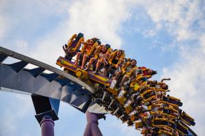 People riding inverted roller coaster against blue sky