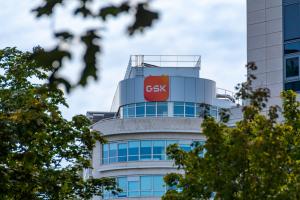 GSK logo on curved building behind trees.