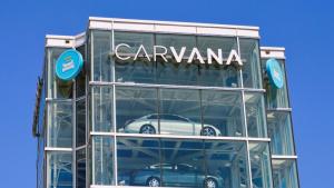 Glass Carvana tower with parked cars, branded signage, and clear blue sky.