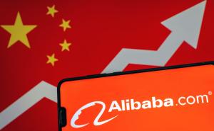 Alibaba logo on smartphone and blurred screen with flag of China with arrow at the background.