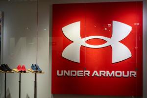 The Under Armour logo and shoes are pictured. Under Armour is a manufacturer of shoes, clothing, and athletic apparel.
