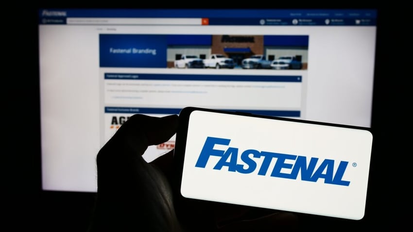 Person holding cellphone with logo of US distribution business Fastenal Company on screen in front of webpage.