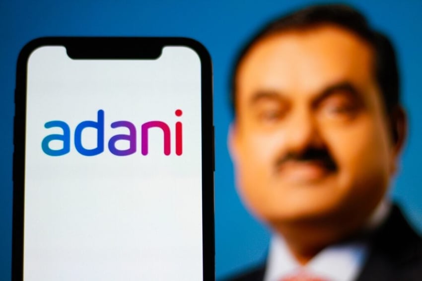Adani corp is displayed on a smartphone with CEO Gautam Adani in the background.