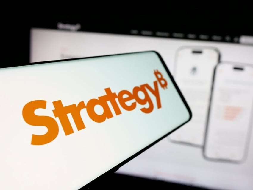 Smartphone with logo of US company MicroStrategy Inc. on screen in front of website. Focus on center-left of phone display