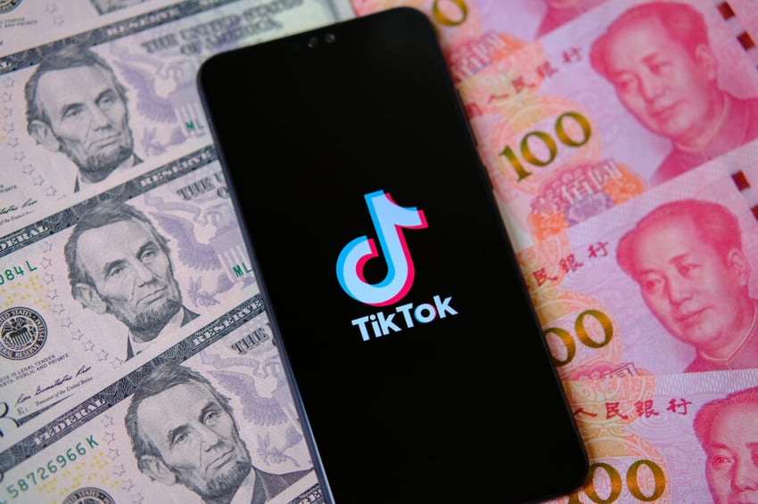 Stone UK - August 1 2020: TikTok logo seen on a smartphone surrounded by US dollars and Chinese Yuan banknotes. Concept for TikTok being in centre of American - Chinese trade war.